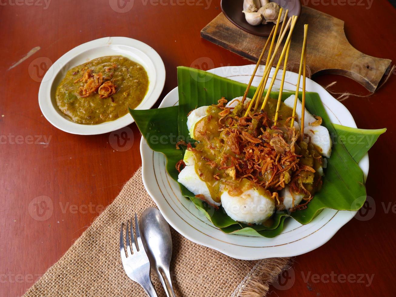 Sate Padang or satay padang is Spicy beef satay from Padang, West Sumatra. Served with spicy curry sauce and rice cake, lontong on banana leaf. isolated on white background photo