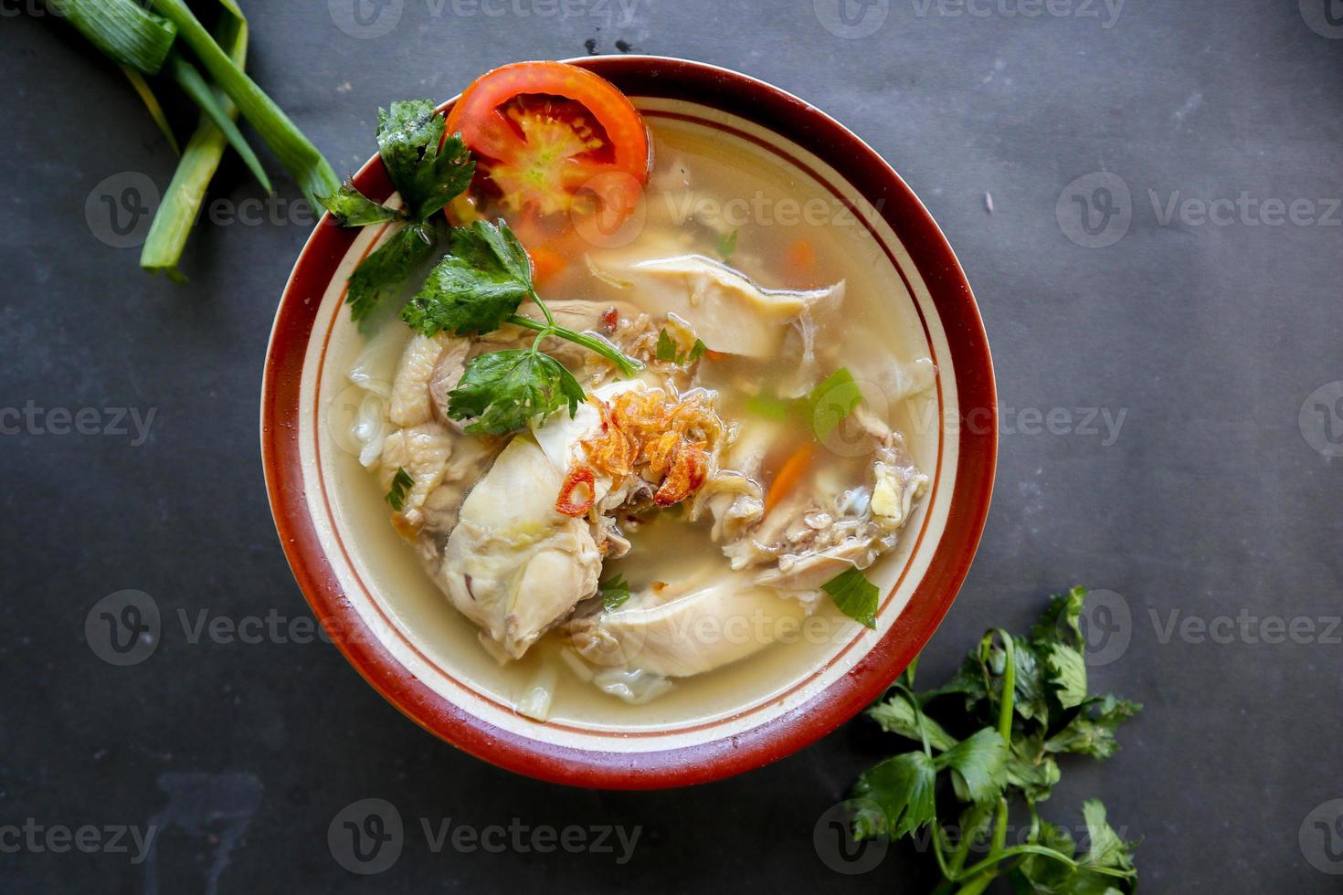 Chicken soup served with vegetables, tomatoes, celery in a bowl, spoon and fork. with black background photo