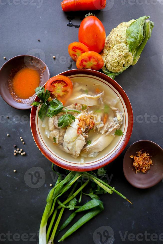 Chicken soup served with vegetables, tomatoes, celery in a bowl, spoon and fork. with black background photo