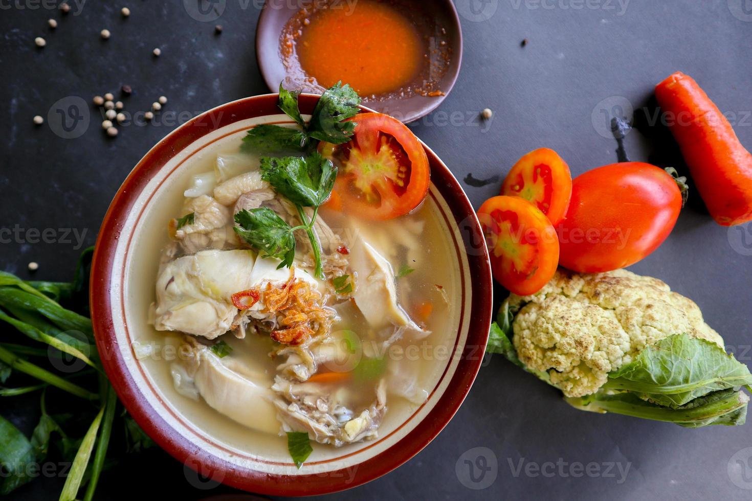 Chicken soup served with vegetables, tomatoes, celery in a bowl, spoon and fork. with black background photo