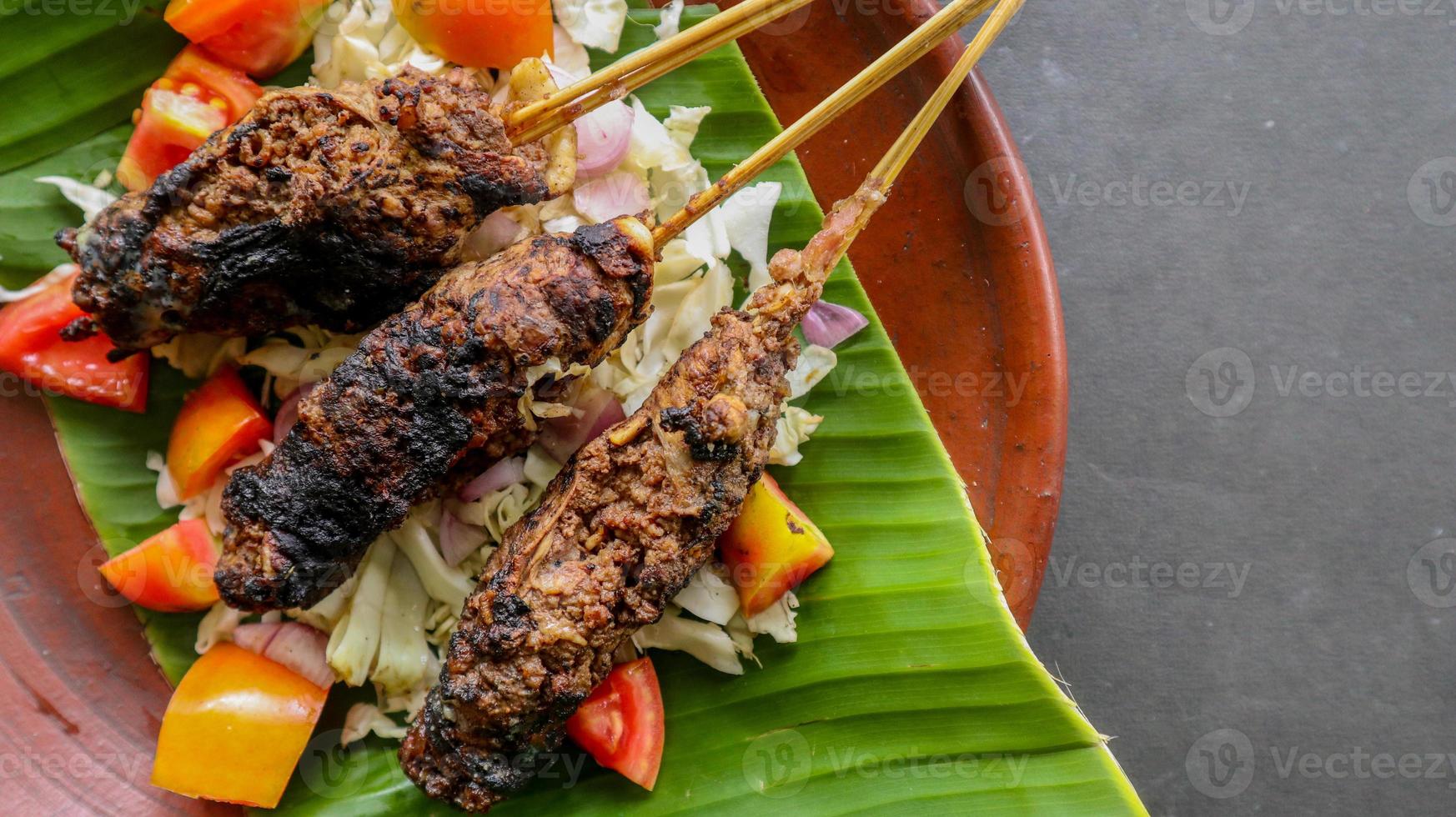 sate buntel or satay buntel is satay made from minced mutton wrapped in mutton fat and then grilled. seasoning with tomatoes, shallots, pepper, cabbage photo