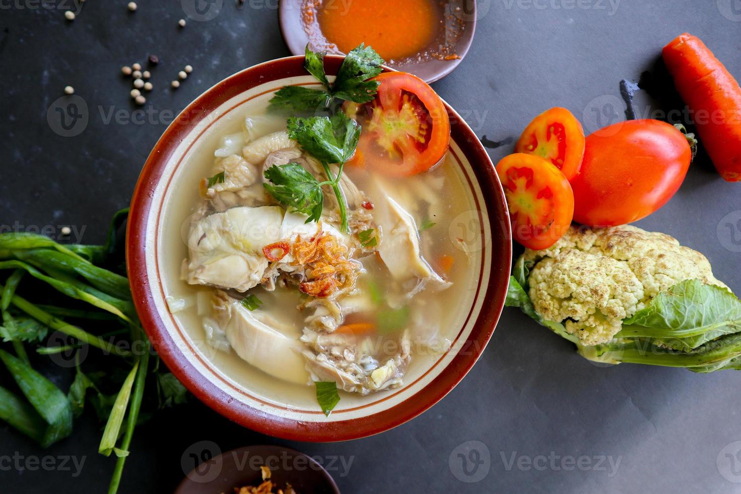 Chicken soup served with vegetables, tomatoes, celery in a bowl, spoon and fork. with black background photo