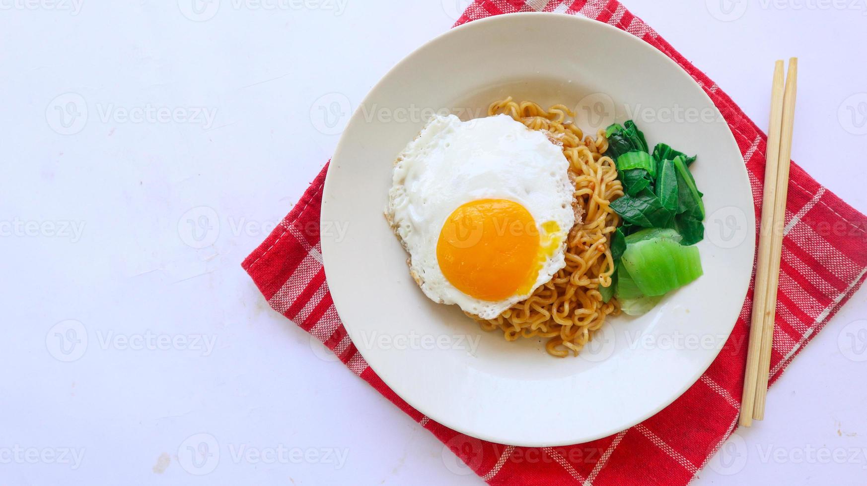 instant noodles served with egg fried and mustard greens on plate. instant fried noodle indomie photo