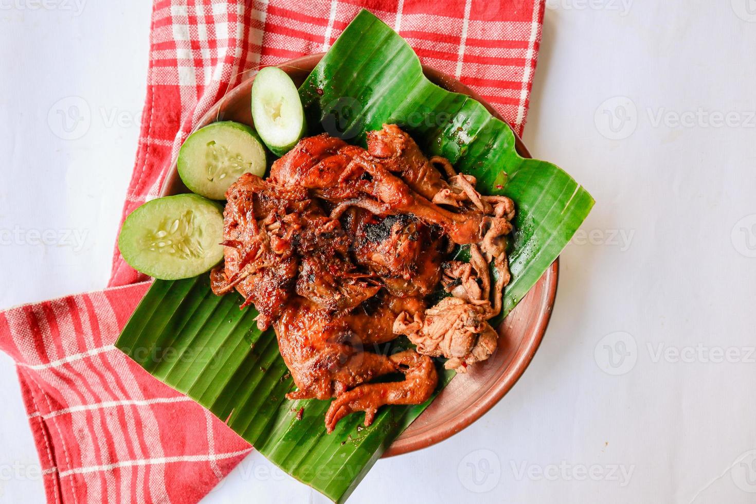 grilled chicken or ayam bakar with cucumber slash served on banana leaf and plate. ayam bakar is traditional grilled chicken from indonesia photo