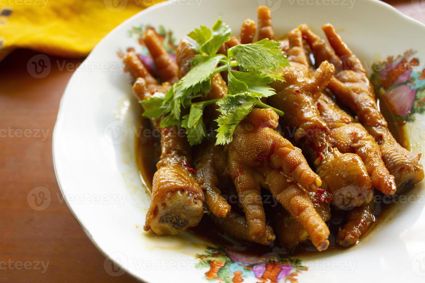 Spicy chicken feet with celery, chili, onion, garlic served with a white plate isolated from a black background. photo