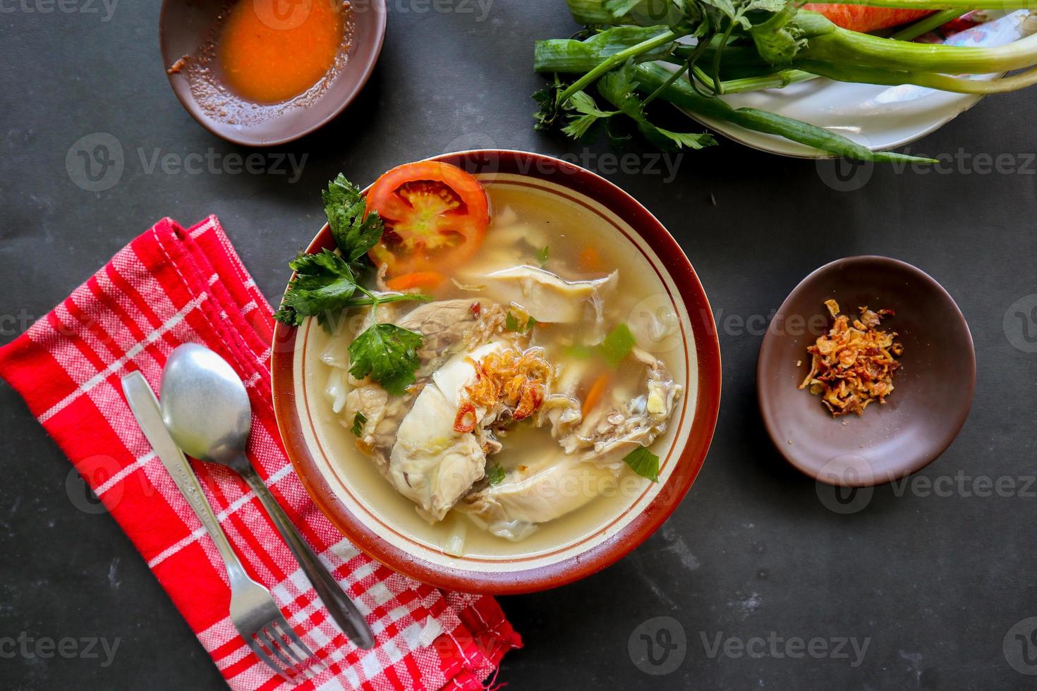 Chicken soup served with vegetables, tomatoes, celery in a bowl, spoon and fork. with black background photo