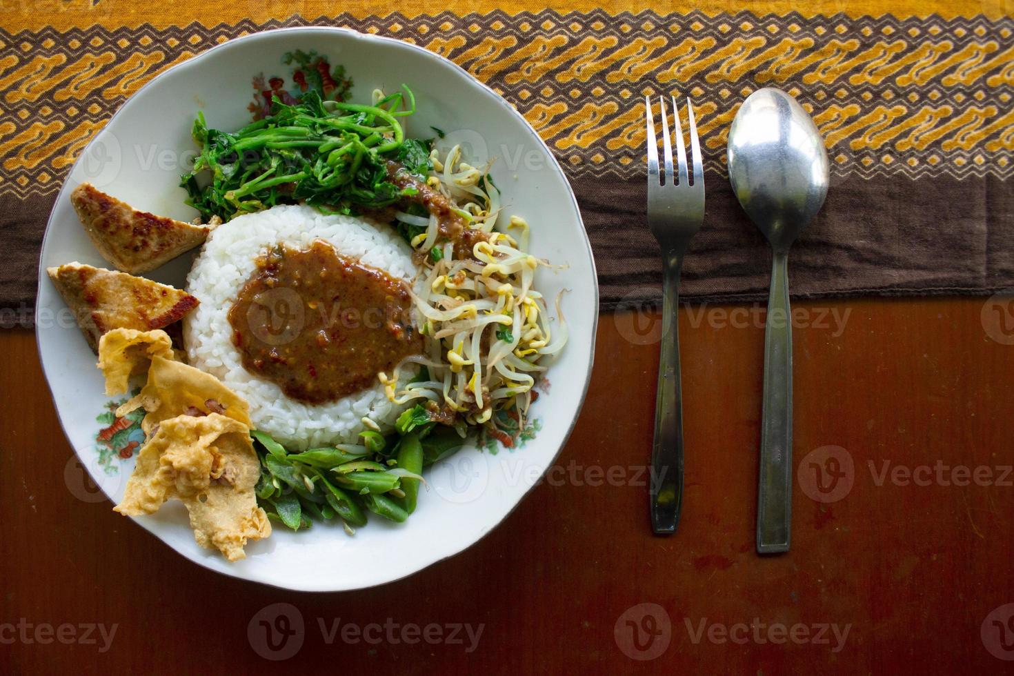 Nasi Pecel or sego pecel is Traditional Javanese rice dish of steamed rice with vegetable salad, peanut sauce, tempeh, tofu bean sprouts and crackers or peyek kacang. on black backgroud photo
