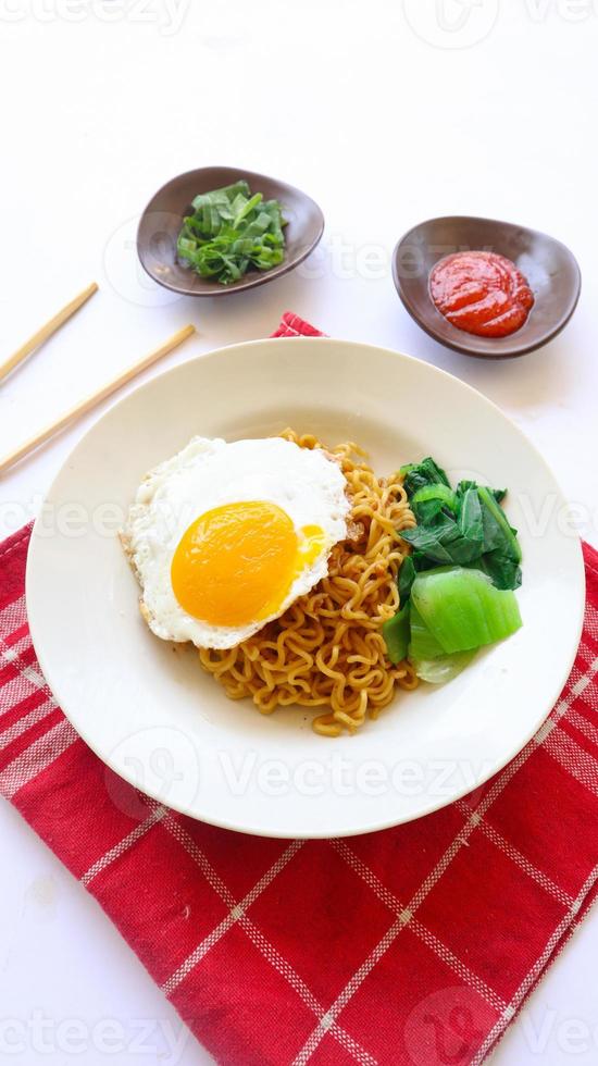 instant noodles served with egg fried and mustard greens on plate. instant fried noodle indomie photo