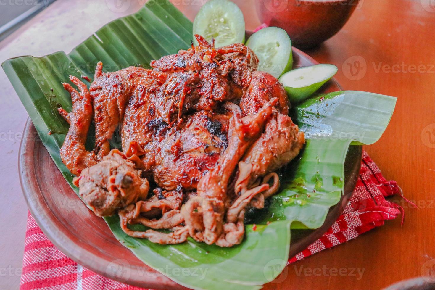 grilled chicken or ayam bakar with cucumber slash served on banana leaf and plate. ayam bakar is traditional grilled chicken from indonesia photo