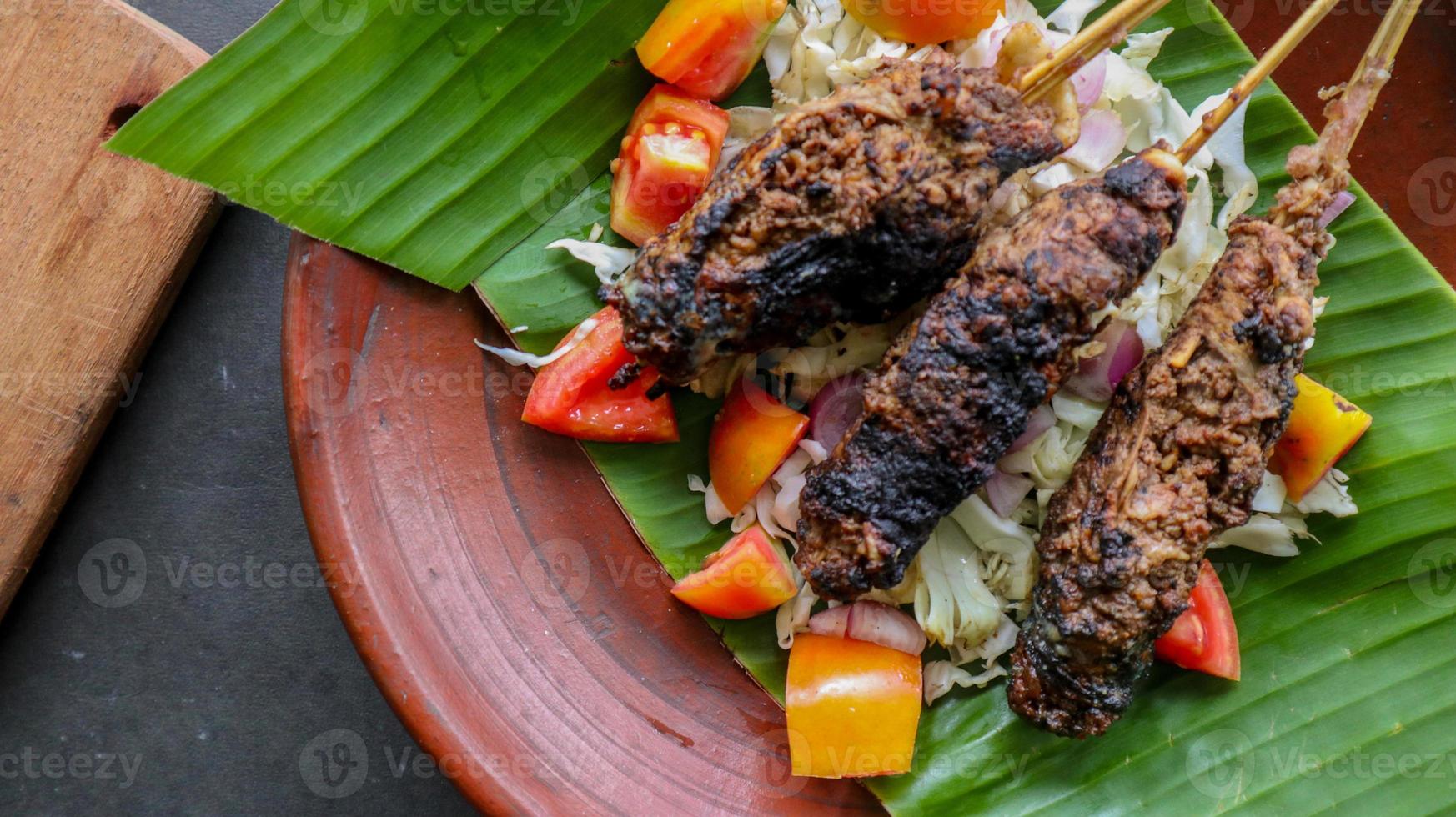 sate buntel or satay buntel is satay made from minced mutton wrapped in mutton fat and then grilled. seasoning with tomatoes, shallots, pepper, cabbage photo