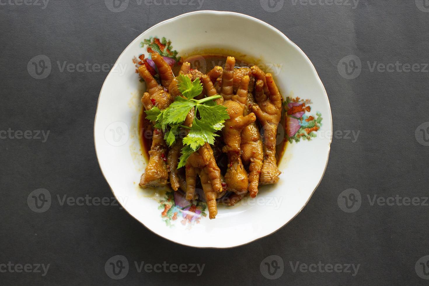 Spicy chicken feet with celery, chili, onion, garlic served with a white plate isolated from a black background. photo