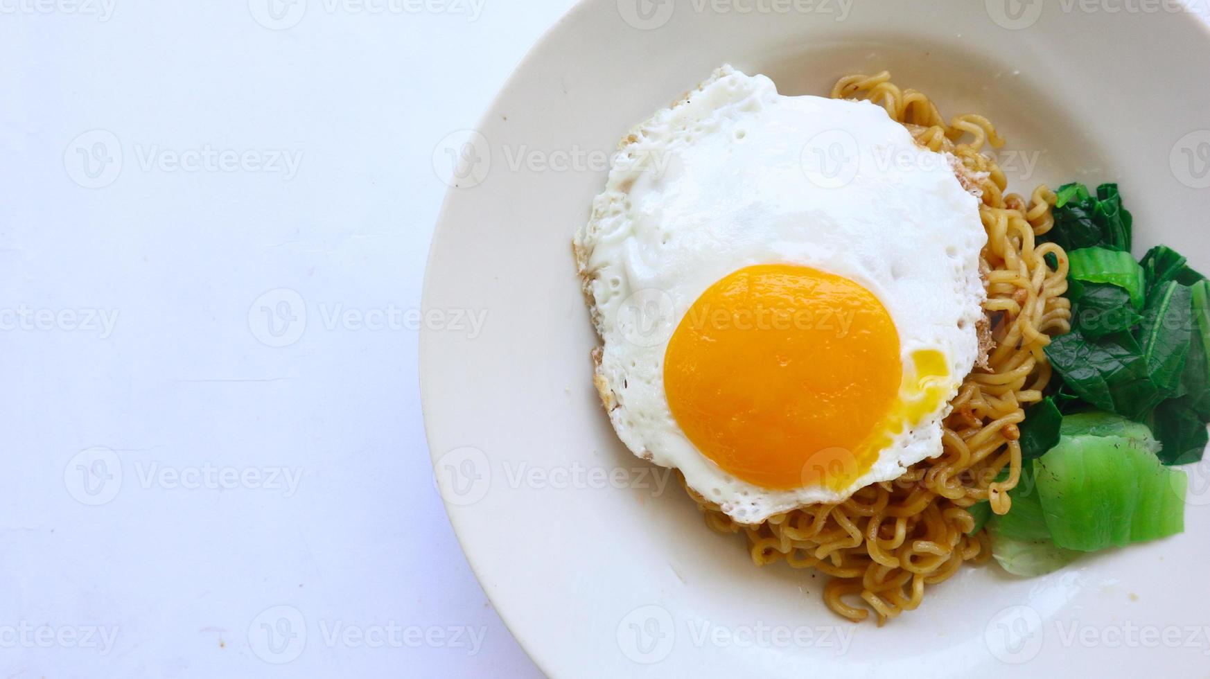 instant noodles served with egg fried and mustard greens on plate. instant fried noodle indomie photo