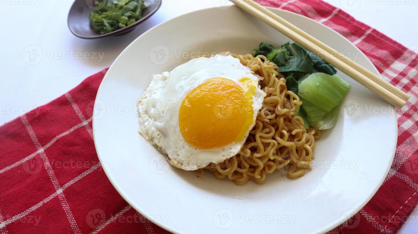 instant noodles served with egg fried and mustard greens on plate. instant fried noodle indomie photo