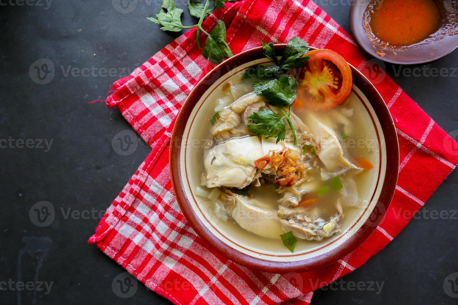Chicken soup served with vegetables, tomatoes, celery in a bowl, spoon and fork. with black background photo
