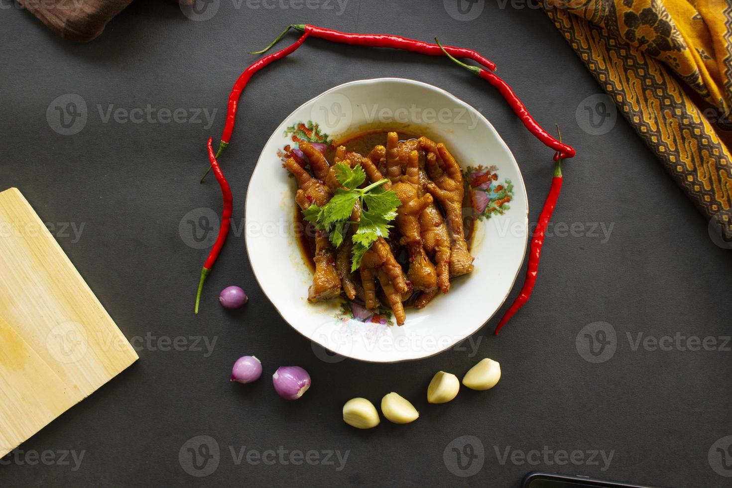 Spicy chicken feet with celery, chili, onion, garlic served with a white plate isolated from a black background. photo