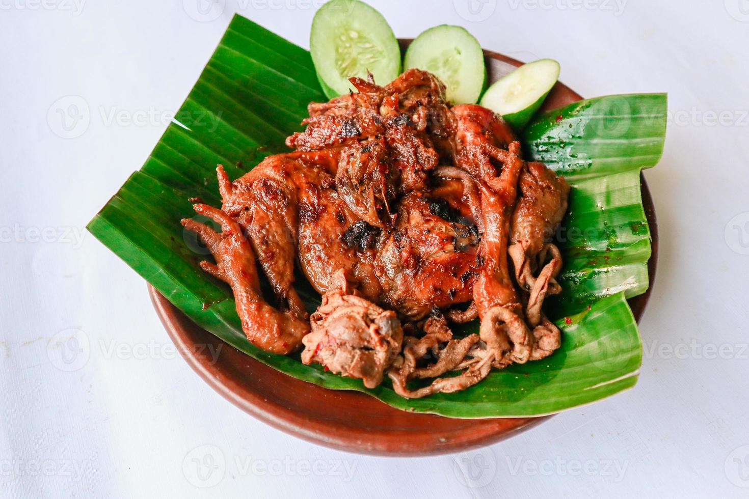 grilled chicken or ayam bakar with cucumber slash served on banana leaf and plate. ayam bakar is traditional grilled chicken from indonesia photo