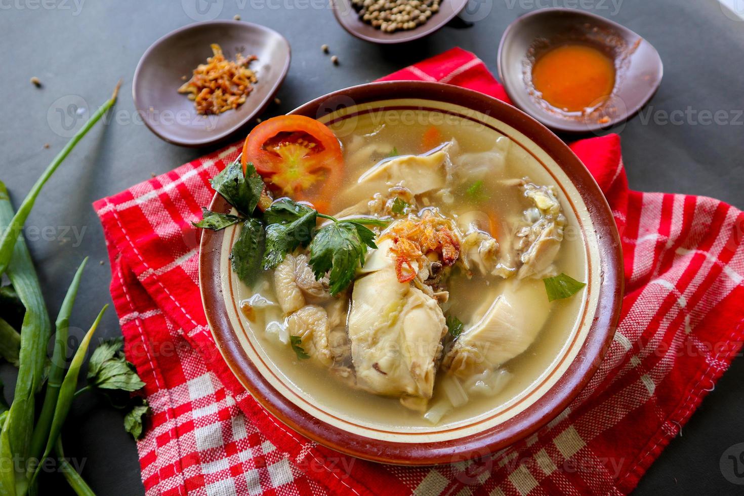 Chicken soup served with vegetables, tomatoes, celery in a bowl, spoon and fork. with black background photo