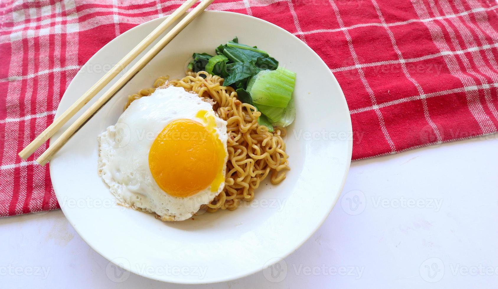 instant noodles served with egg fried and mustard greens on plate. instant fried noodle indomie photo