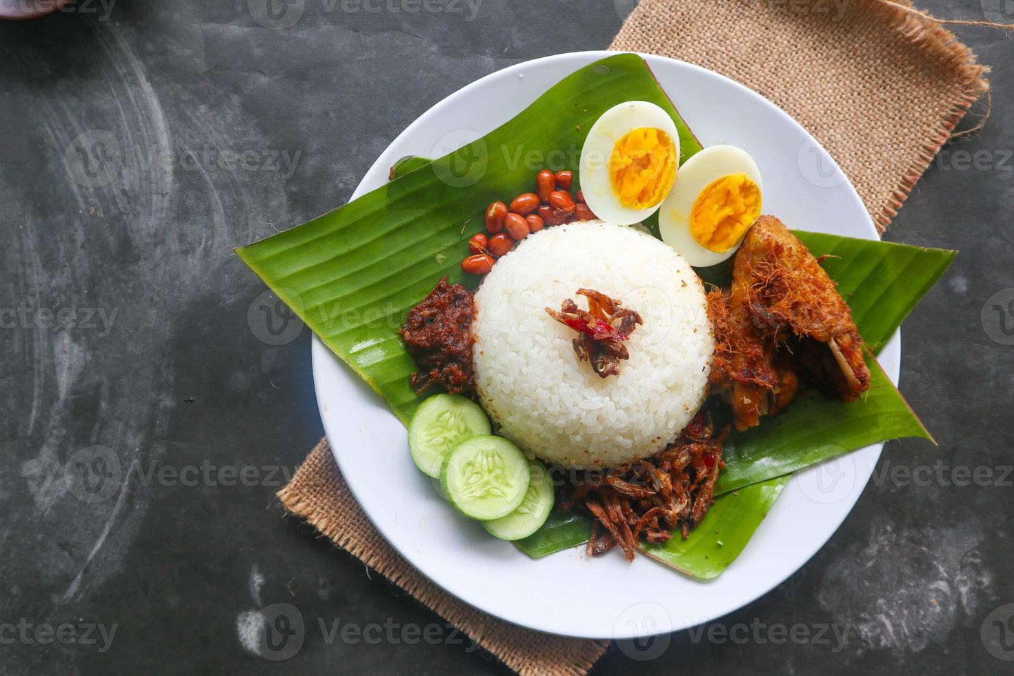 nasi lemak, is traditional malay made boiled eggs, beans, anchovies, chili sauce, cucumber. from dish served on a banana leaf photo