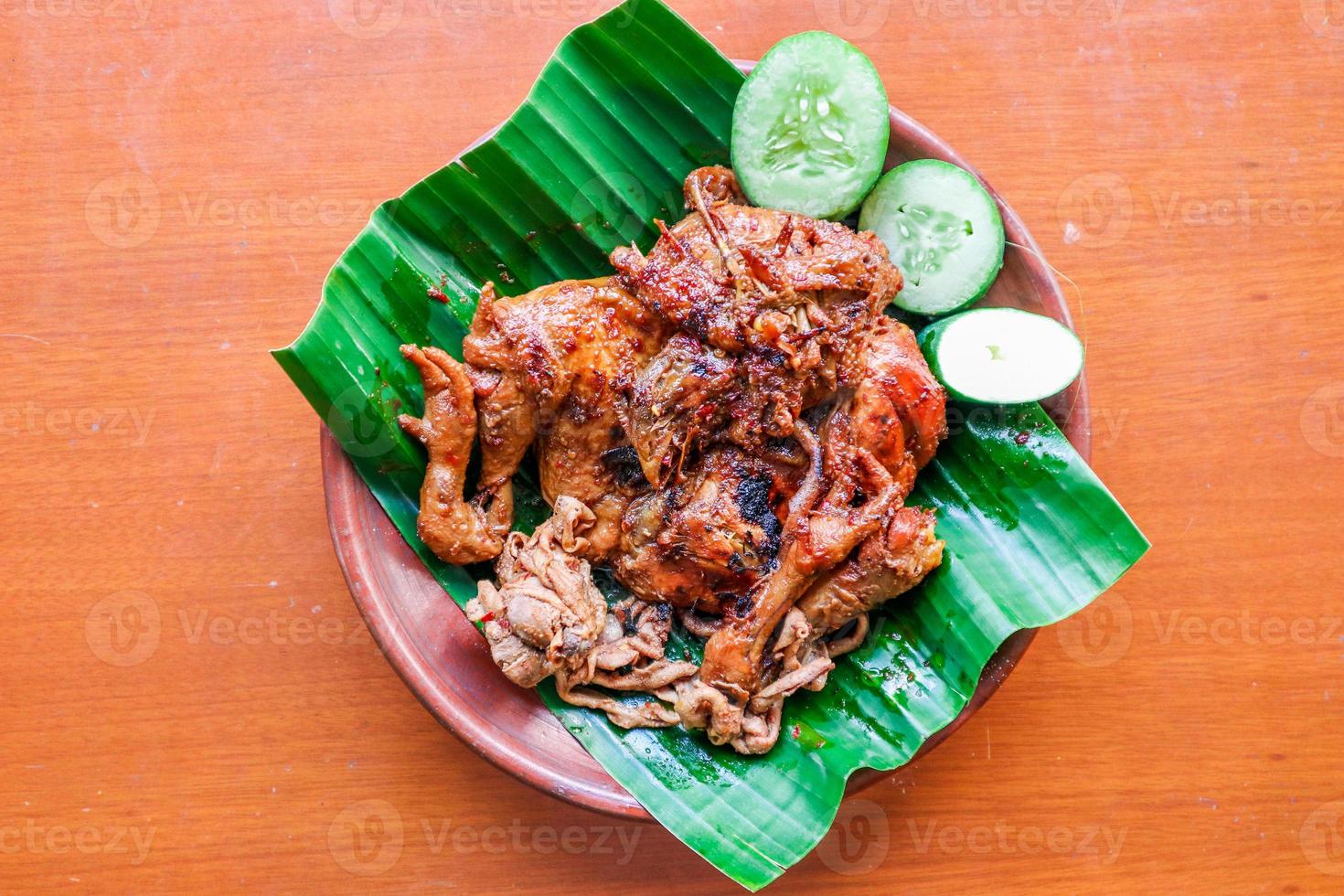 grilled chicken or ayam bakar with cucumber slash served on banana leaf and plate. ayam bakar is traditional grilled chicken from indonesia photo