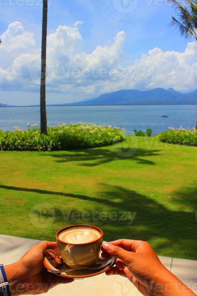 holding cappuccino coffee in the morning on the beach when the blue sky is bright photo