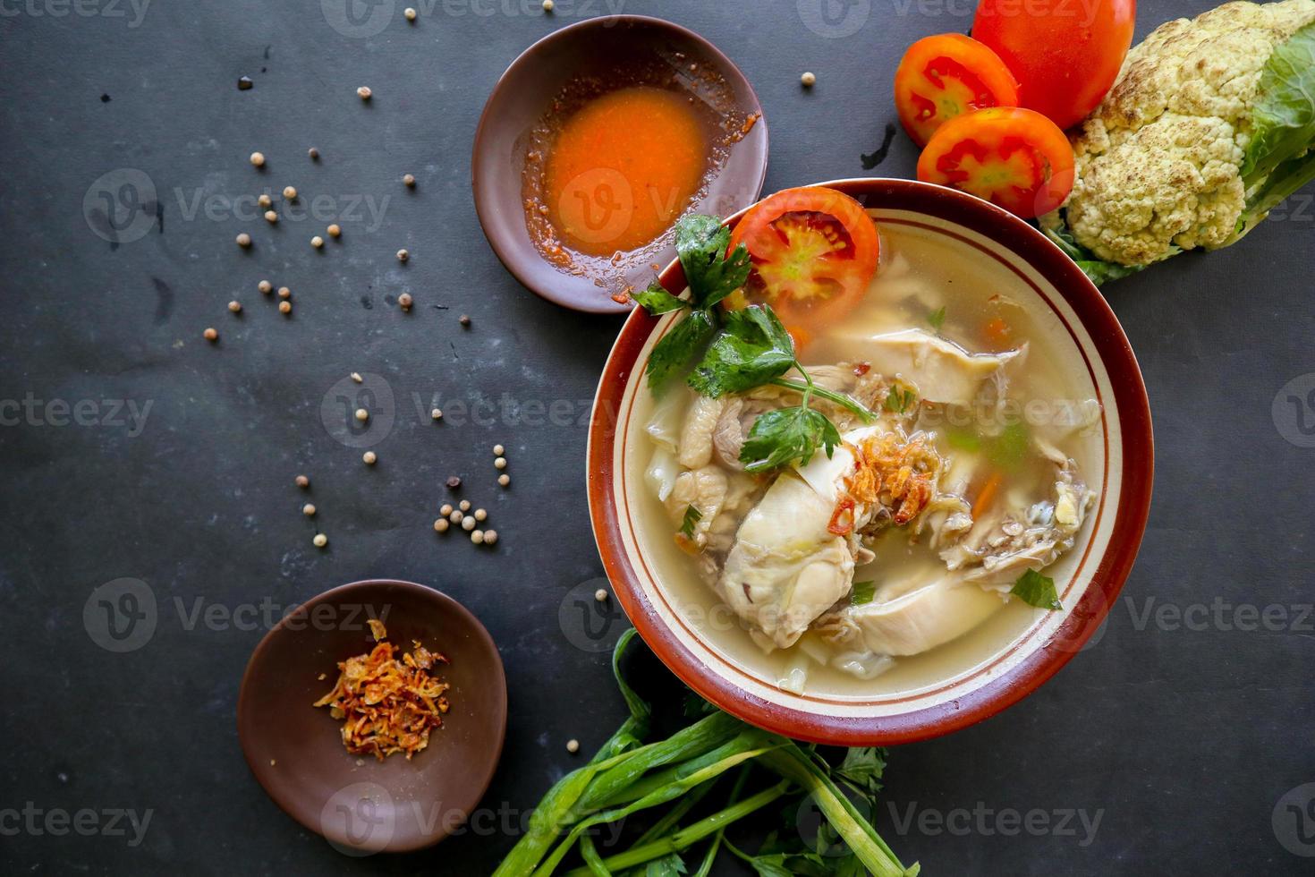 Chicken soup served with vegetables, tomatoes, celery in a bowl, spoon and fork. with black background photo