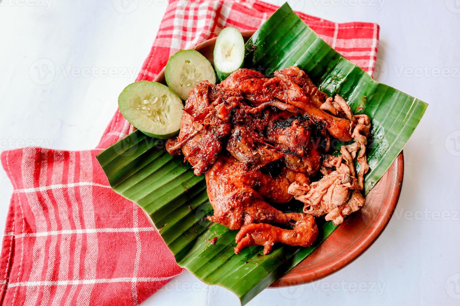 grilled chicken or ayam bakar with cucumber slash served on banana leaf and plate. ayam bakar is traditional grilled chicken from indonesia photo