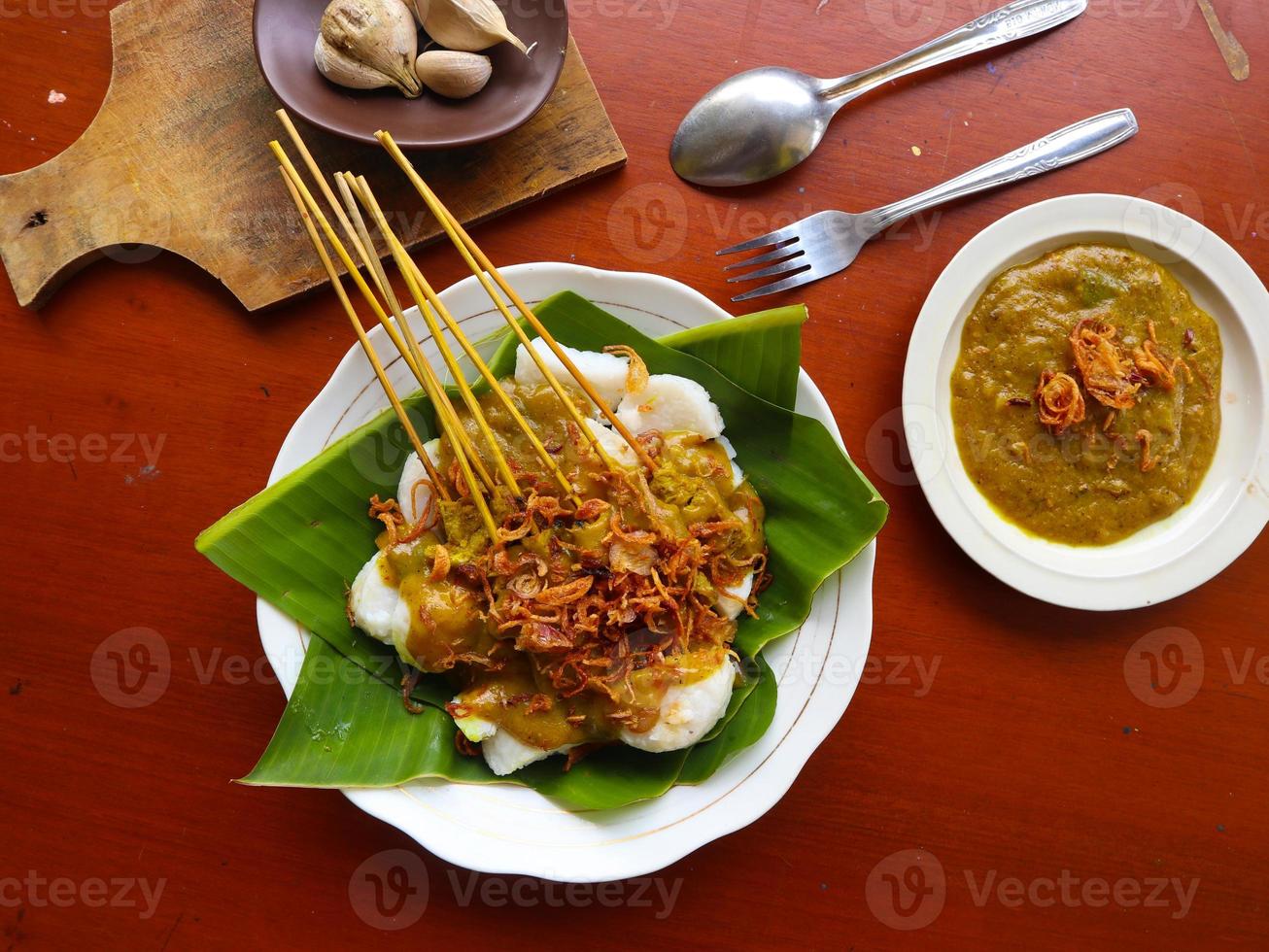 Sate Padang or satay padang is Spicy beef satay from Padang, West Sumatra. Served with spicy curry sauce and rice cake, lontong on banana leaf. isolated on white background photo