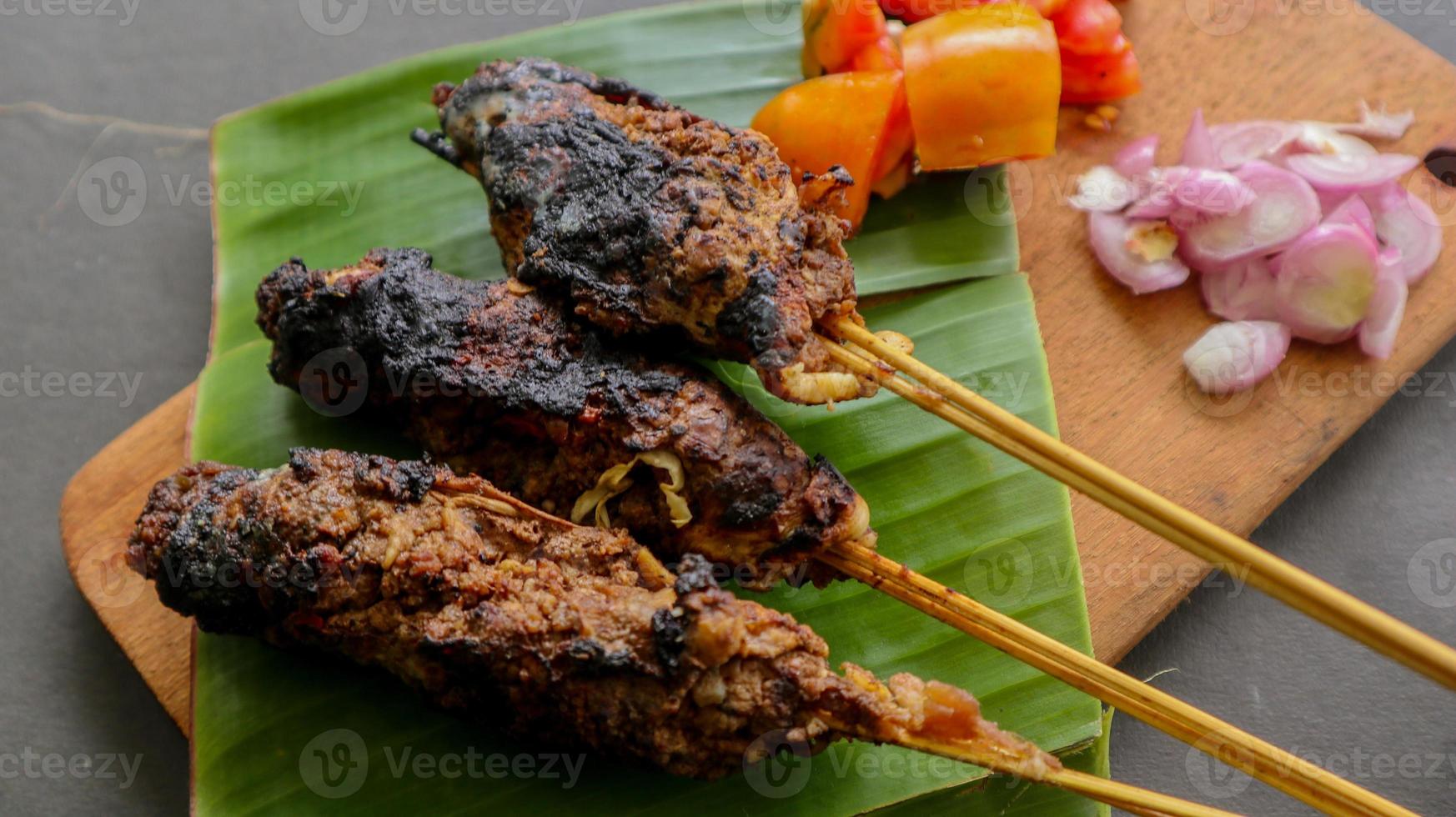 sate buntel o satay buntel es satay hecho de cordero picado envuelto en grasa de cordero y luego asado a la parrilla. condimento con tomates, chalotes, pimienta, repollo foto