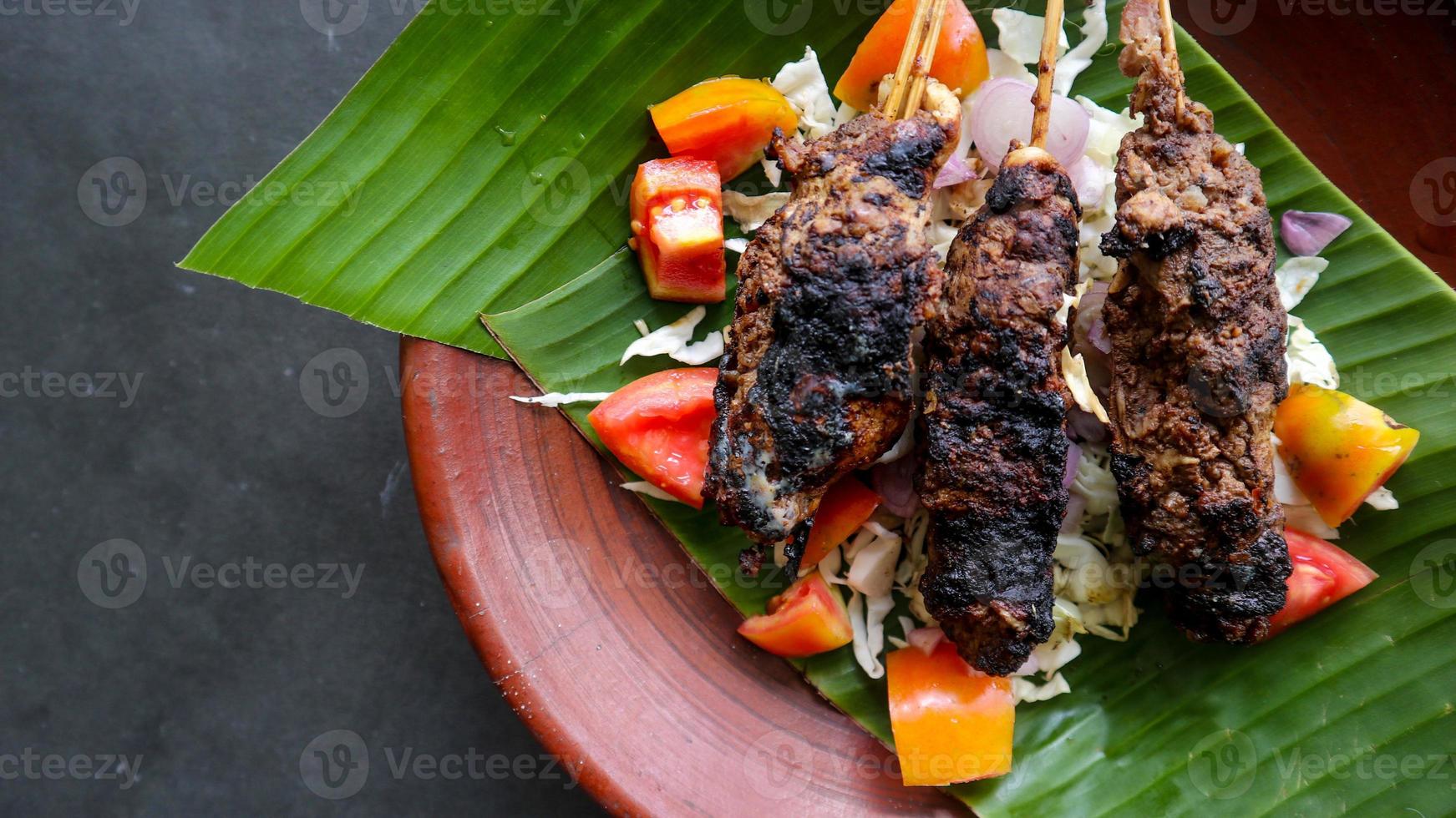 sate buntel o satay buntel es satay hecho de cordero picado envuelto en grasa de cordero y luego asado a la parrilla. condimento con tomates, chalotes, pimienta, repollo foto