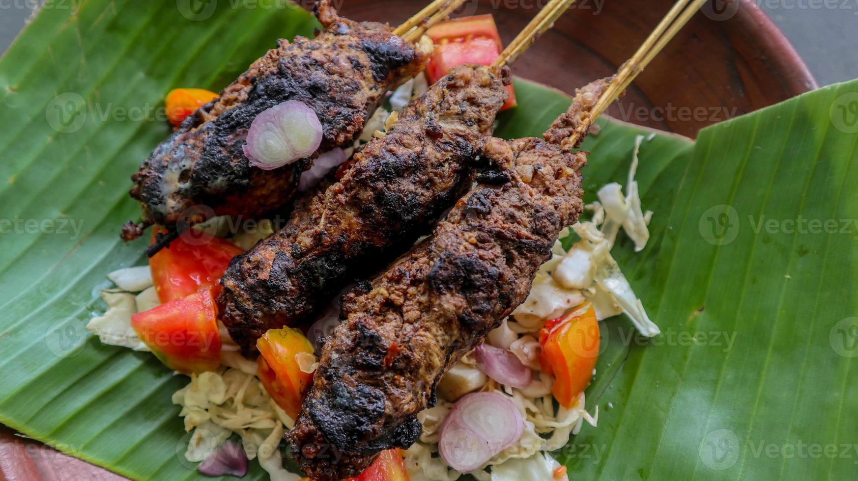 sate buntel o satay buntel es satay hecho de cordero picado envuelto en grasa de cordero y luego asado a la parrilla. condimento con tomates, chalotes, pimienta, repollo foto