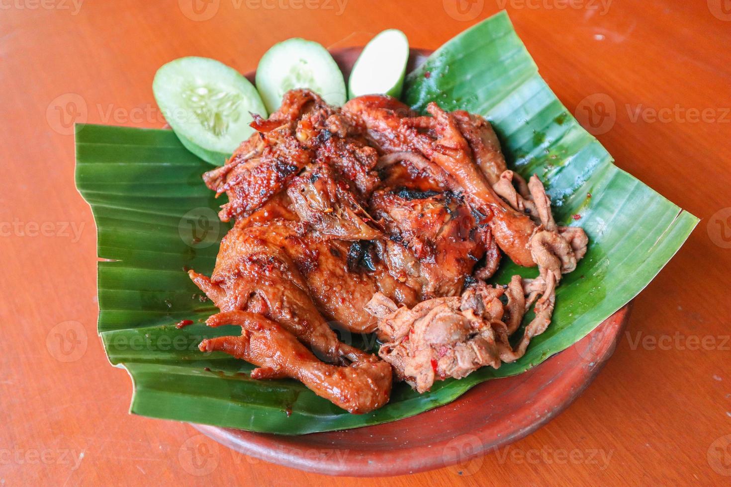 grilled chicken or ayam bakar with cucumber slash served on banana leaf and plate. ayam bakar is traditional grilled chicken from indonesia photo