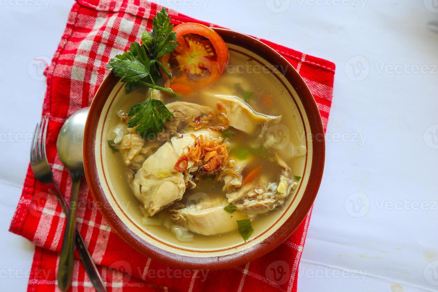 Chicken soup served with vegetables, tomatoes, celery in a bowl, spoon and fork. with black background photo