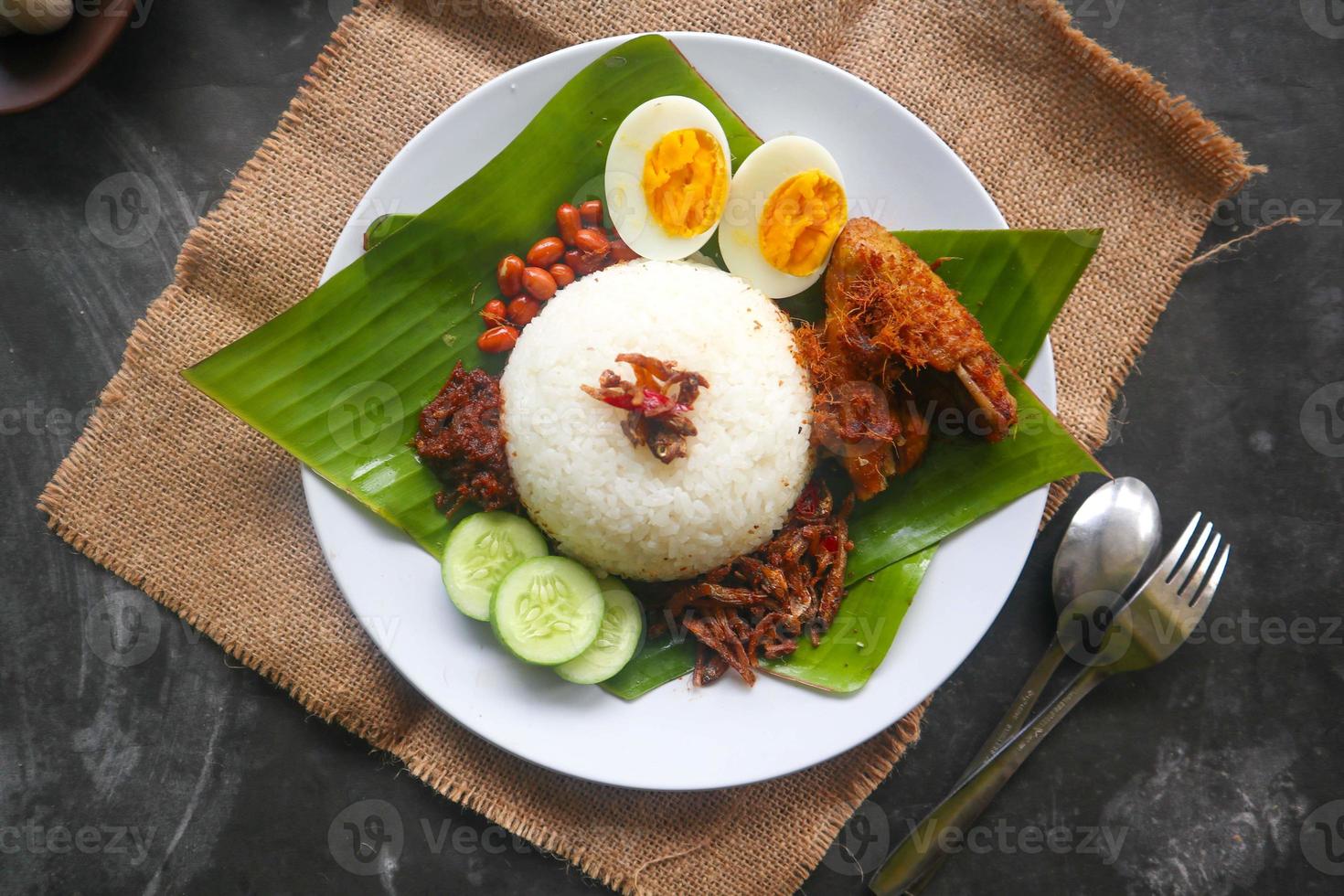 nasi lemak, is traditional malay made boiled eggs, beans, anchovies, chili sauce, cucumber. from dish served on a banana leaf photo