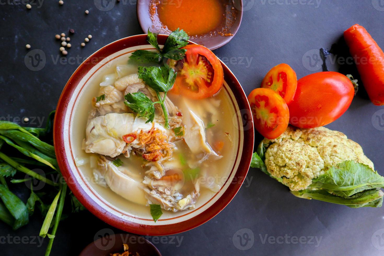 Chicken soup served with vegetables, tomatoes, celery in a bowl, spoon and fork. with black background photo
