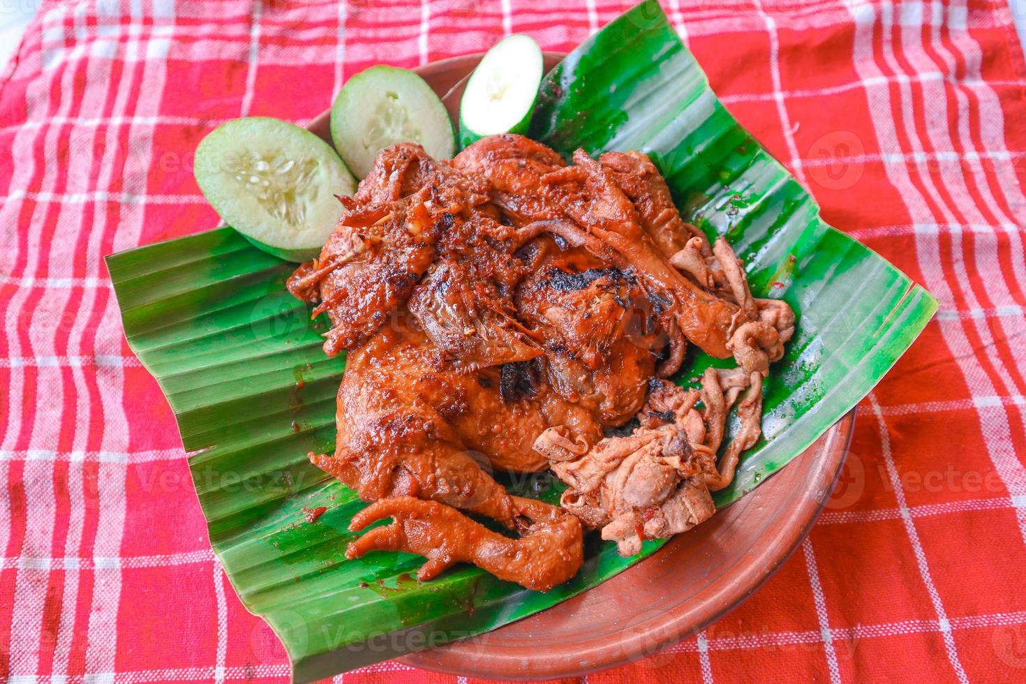 grilled chicken or ayam bakar with cucumber slash served on banana leaf and plate. ayam bakar is traditional grilled chicken from indonesia photo