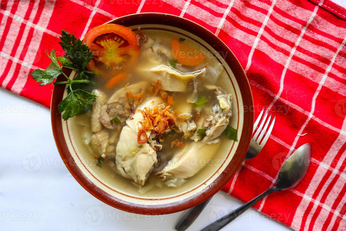 Chicken soup served with vegetables, tomatoes, celery in a bowl, spoon and fork. with black background photo