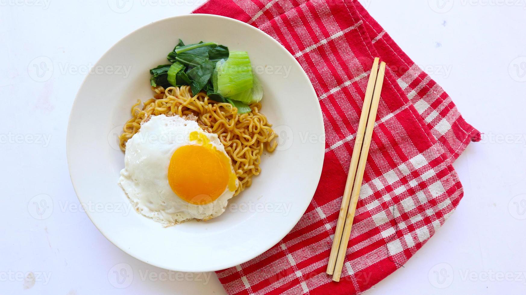 instant noodles served with egg fried and mustard greens on plate. instant fried noodle indomie photo