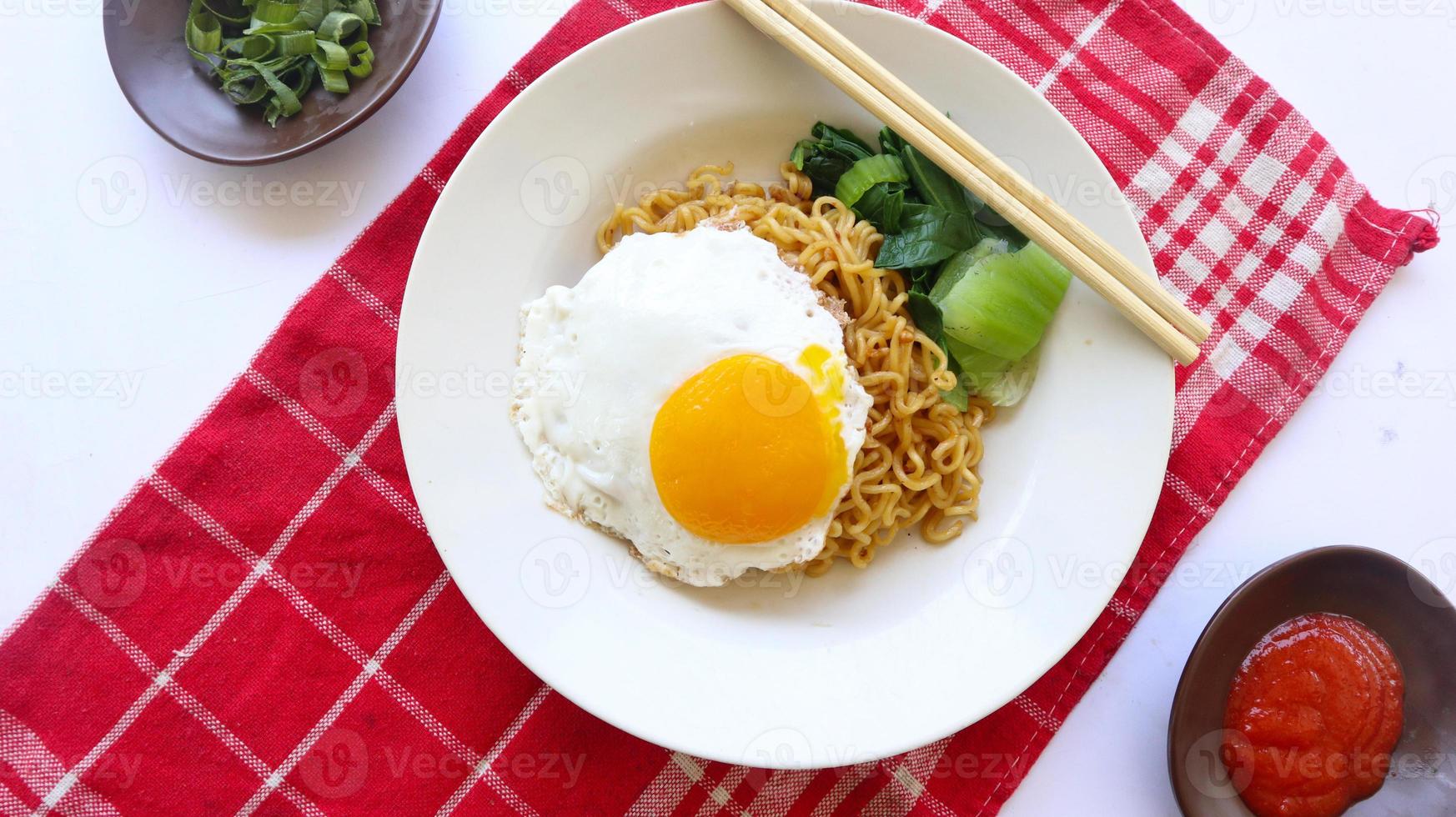 instant noodles served with egg fried and mustard greens on plate. instant fried noodle indomie photo
