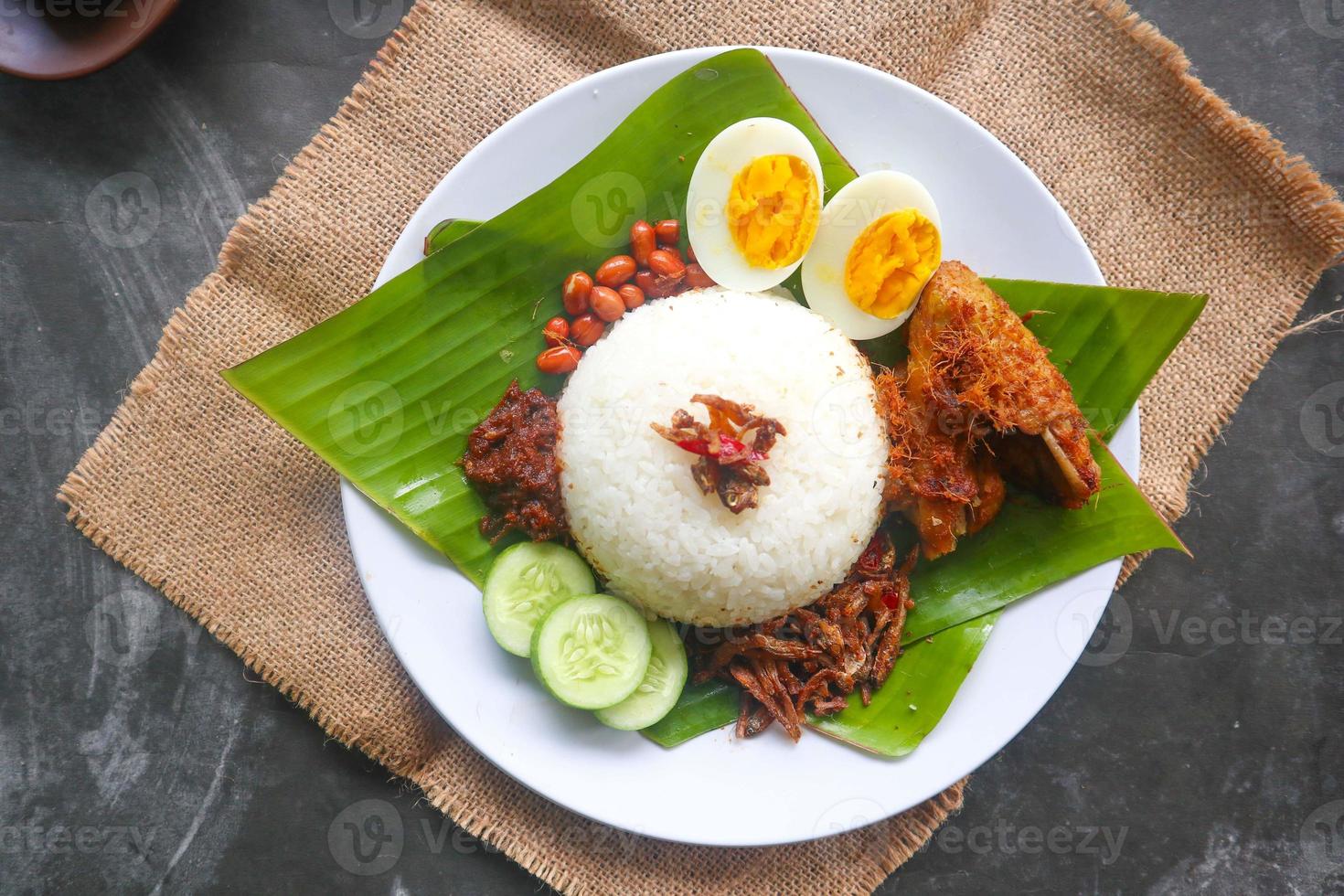 nasi lemak, is traditional malay made boiled eggs, beans, anchovies, chili sauce, cucumber. from dish served on a banana leaf photo