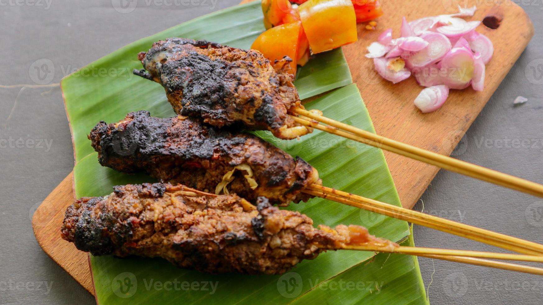 sate buntel o satay buntel es satay hecho de cordero picado envuelto en grasa de cordero y luego asado a la parrilla. condimento con tomates, chalotes, pimienta, repollo foto