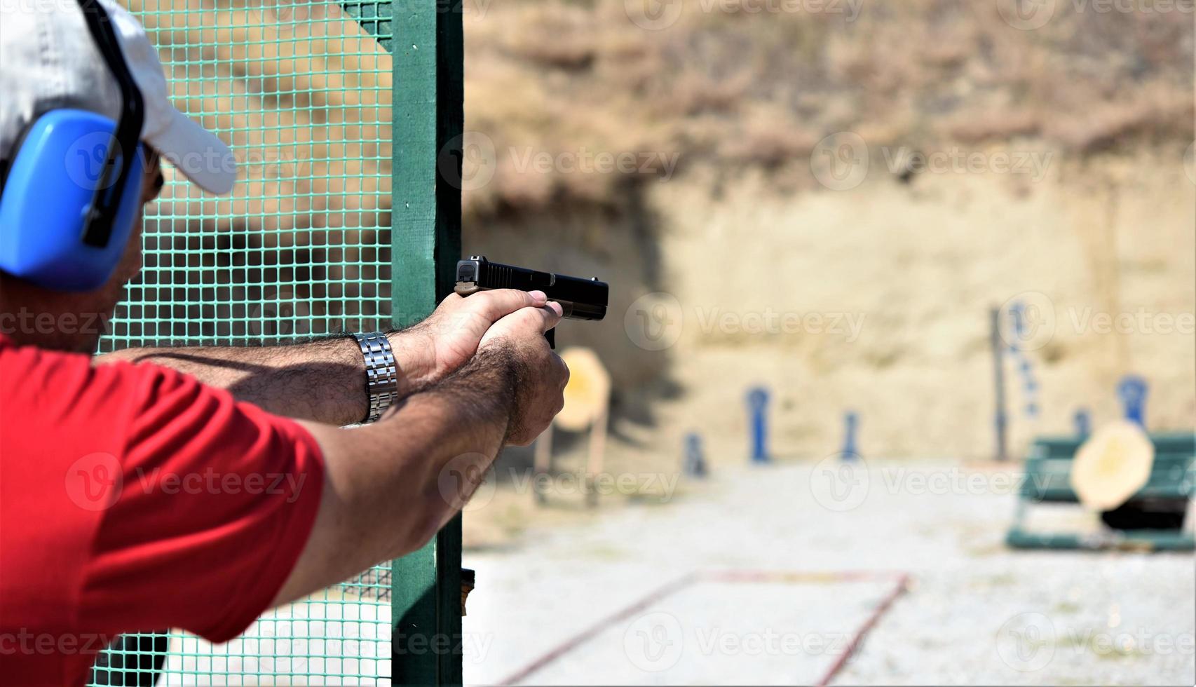 vista trasera de un hombre disparando su arma en un rancho de práctica. foto