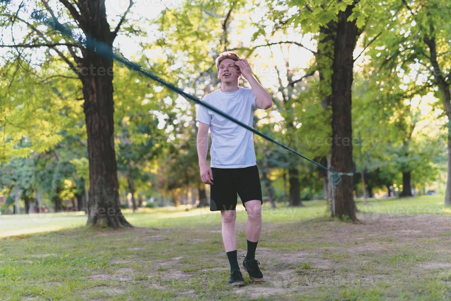 Young man balancing and jumping on slackline. Man walking, jumping and balancing on rope in park. photo