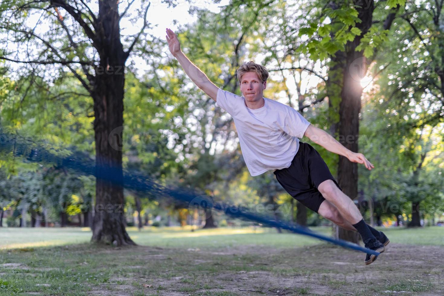 Young man balancing and jumping on slackline. Man walking, jumping and balancing on rope in park. photo