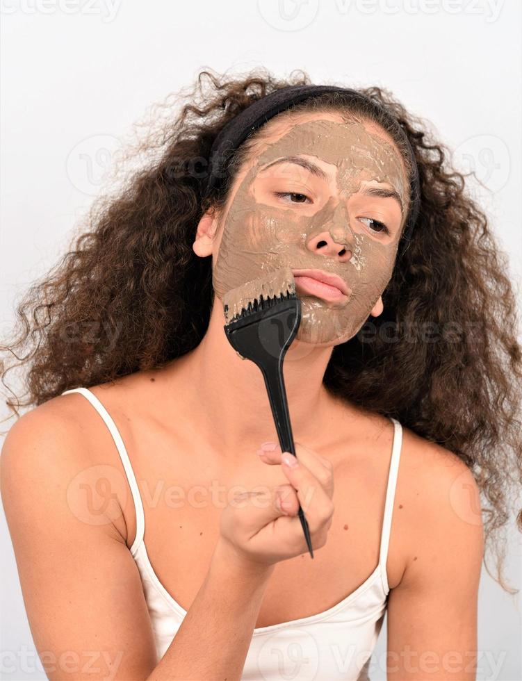 Beauty procedures skin care concept. Young woman applying facial gray mud clay mask to her face photo