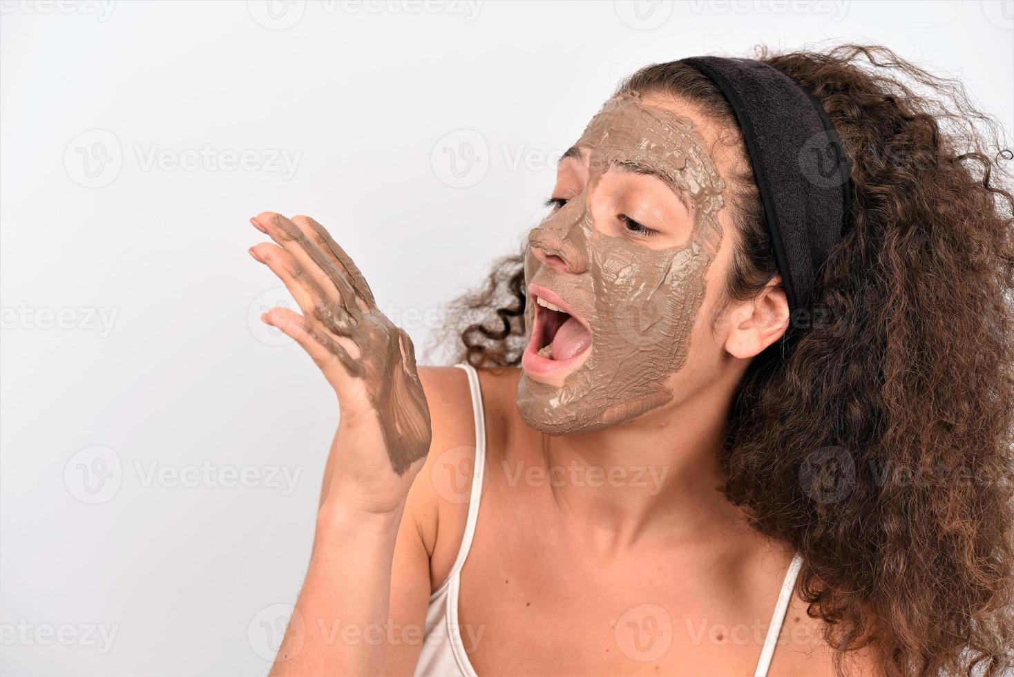 Beauty procedures skin care concept. Young woman applying facial gray mud clay mask to her face photo