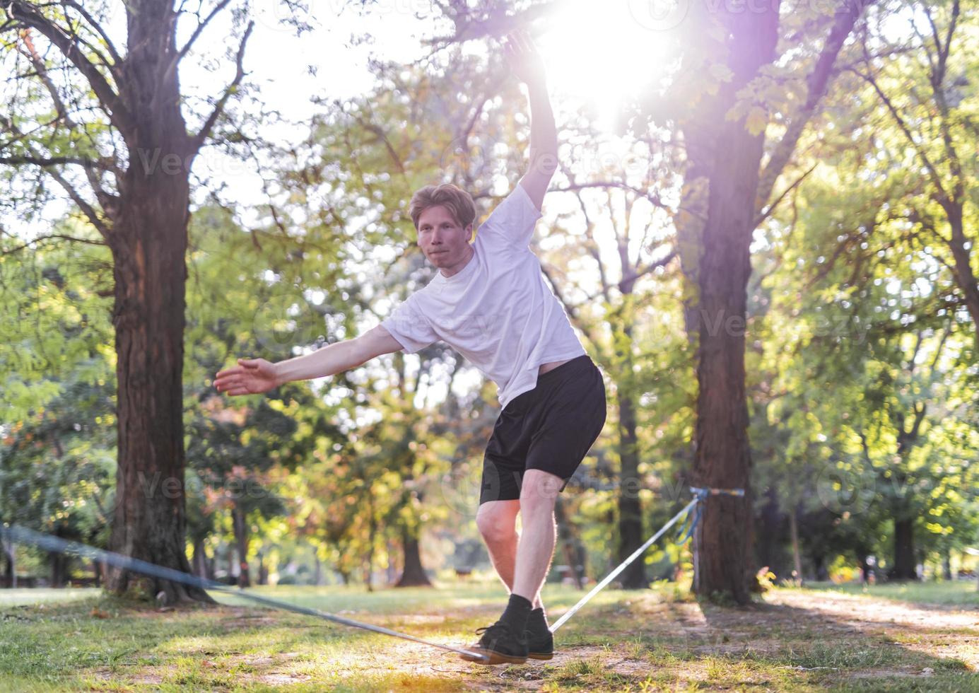 Young man balancing and jumping on slackline. Man walking, jumping and balancing on rope in park. photo