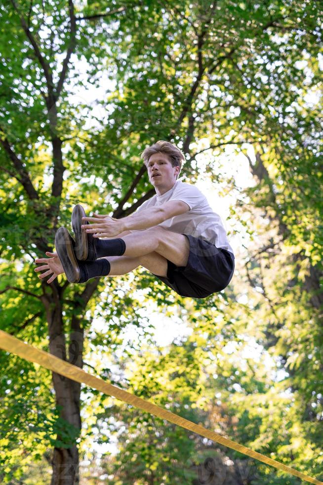 Young man balancing and jumping on slackline. Man walking, jumping and balancing on rope in park. photo