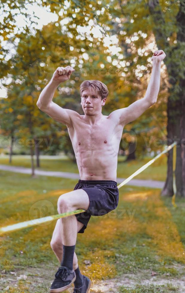 Young man balancing and jumping on slackline. Man walking, jumping and balancing on rope in park. photo