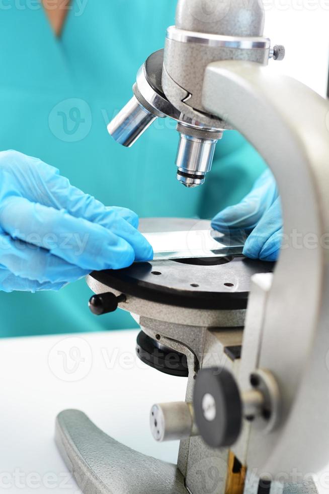 científico con guantes médicos azules y muestras uniformes de aprendizaje covid-19 con microscopio en laboratorio. foto